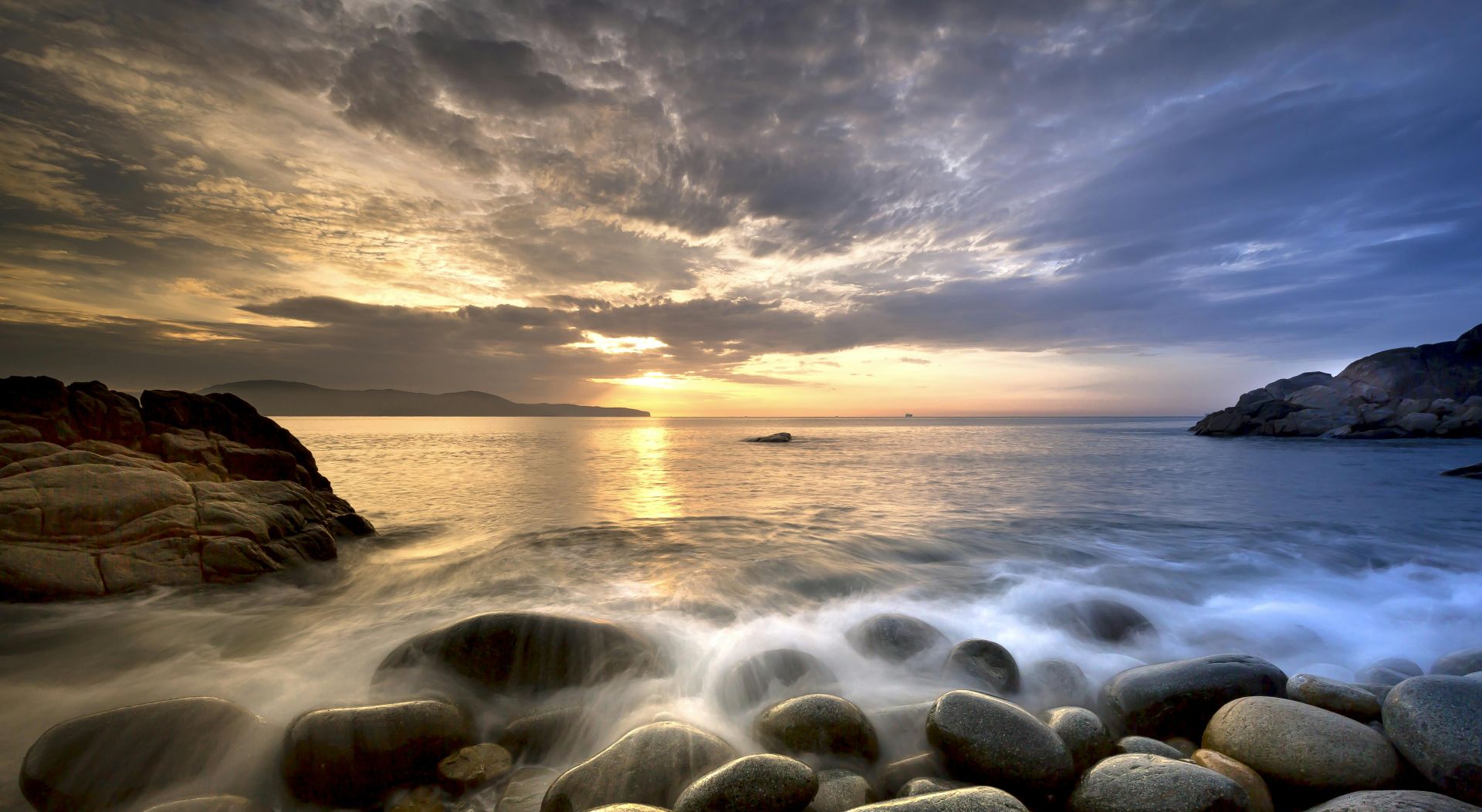 Picturesque scenery of cloudy sky and big heavy stones and rocks washing by foamy waves  of ocean at sundown